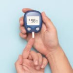 Man using glucometer, checking blood sugar level. Diabetes concept on blue background